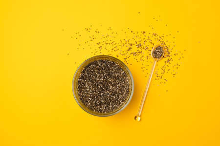 Glass bowl and spoon with chia seed son a bright yellow background, closeup, view from aboveの写真素材