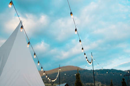 Light bulbs retro garland hanging in restaurant or cafe in the garden at evening time. Lighting decor. Bright blue sky with a cloudsの写真素材