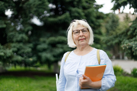 Blonde teacher woman lady 40s 50s years old wearing eyeglasses standing hold notepads looking camera outdoorsの写真素材