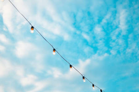 Light bulbs retro garland hanging in restaurant or cafe in the garden at evening time. Lighting decor. Bright blue sky with cloudsの写真素材