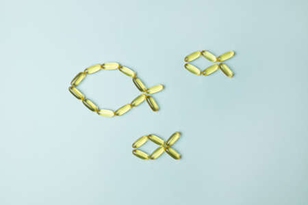 Fish oil omega 3 capsules are arranged in the shape of a fish on blue backgroundの写真素材