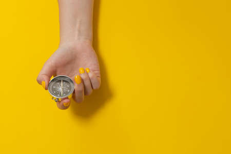 Female hand holding a magnetic compass on a yellow background with copy spaceの写真素材