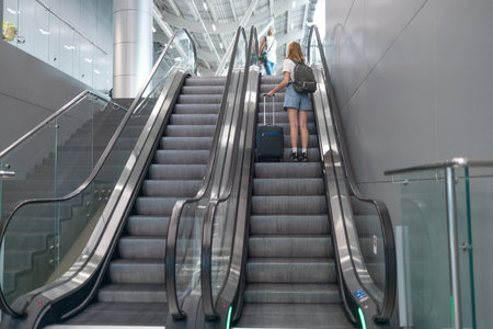 COVID-19 Beauty female tourist with a backpack in airport terminal standing at escalator. Woman passenger traveling by plane transportation during covid19 virus pandemicの写真素材