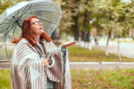 Happy woman walking with transparent umbrella under rain at autumn city park. Wet fall weather season conceptの写真素材