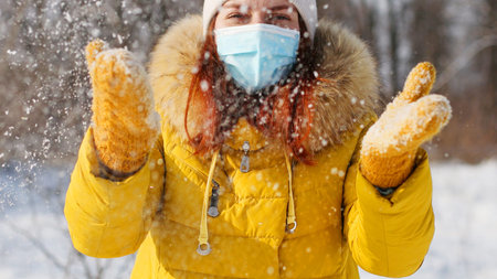 Young woman in bright warm clothes throwing snow in the air at sunny winter day