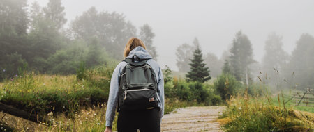 Back view of an active tourist with a backpack travels through a foggy forest
