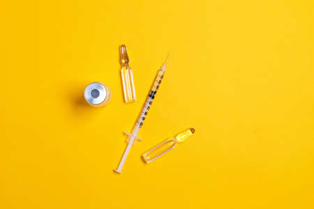 Vaccine in vial and syringe close-up on yellow table background. Medical concept, laboratory, subcutaneous injection vaccination, doseの写真素材