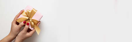 Female hands holding Xmas gift box present with gold bow on gray background. Christmas, New Year minimal greeting card, horizontal holiday banner.の写真素材