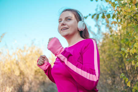 Active sport woman in white wireless headphones running along outdoor in forest park in natureの写真素材