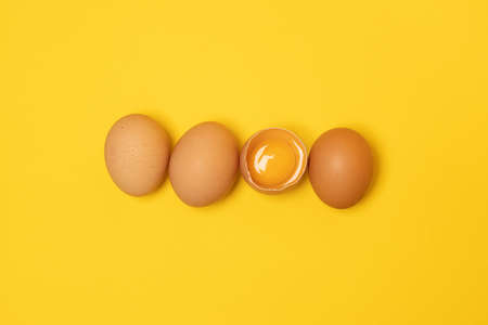 Organic brown chicken eggs and one broken egg with yolk on yellow background. Minimal Easter concept idea.の写真素材
