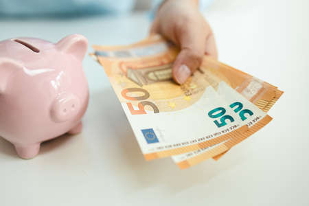 Business piggy bank with a coin on a white table. Man hand holds euro banknotes to pay bills. Business finance saving and investment concept.の写真素材