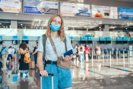 Happy young tourist woman in a protective medical mask holding passport waiting for checking in an...