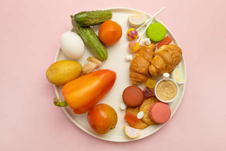 Healthy and unhealthy food. Vegetables and sweets on plate on a pink background. Top view, flat lay. Diet conceptの写真素材
