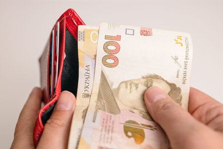 Person hand pulls out hryvnia banknotes from a red wallet to pay for services, loans on white...