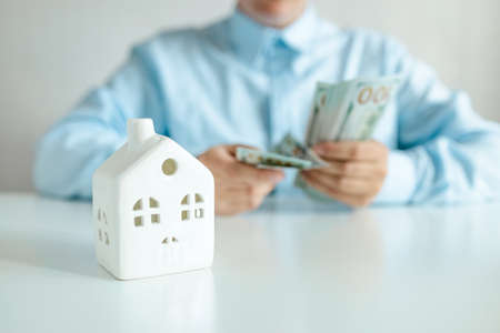 Businesswoman considers a bundle of dollar money. House model on a white table.の写真素材