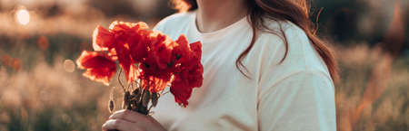 Beutiful young red-haired woman hand holding red poppies bouquet at sunset in the fieldの写真素材