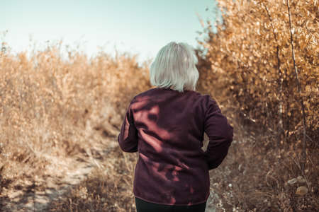 Portrait of a happy active beautiful senior woman running outdoors in the autumn forest in the morningの写真素材