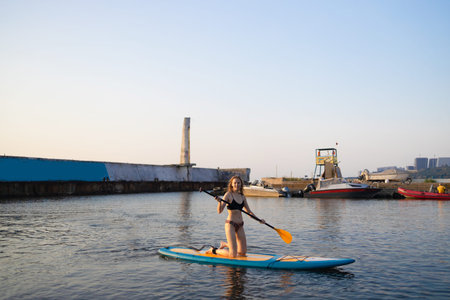 Athletic woman paddling on a SUP sits paddle board in blue water sea on summer day