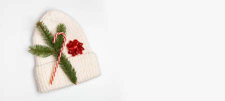 White knitted hat, pine branch and sweet candy cane decor on white background. Christmas, winter, new year concept. Flat lay, top viewの写真素材
