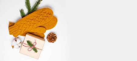 Christmas holiday composition of mustard knitted mittens with xmas gift box and pine cone decor on white background. Winter, new year concept. Flat lay, top viewの写真素材