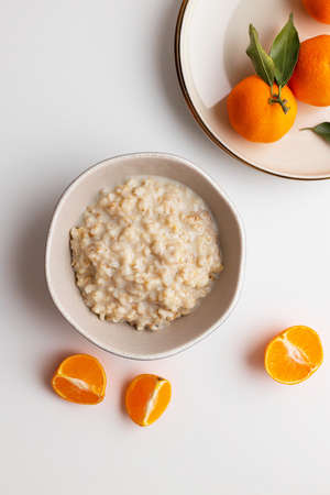 Homemade oatmeal porridge with tangerine or clementin fruits slices on white background. Colorful fruit background. Flat lay, top view, copy space.の写真素材