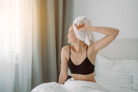 Pretty lady enjoying morning on bed at home. Woman stretching in cozy comfort bed after waking up. Start new dayの写真素材