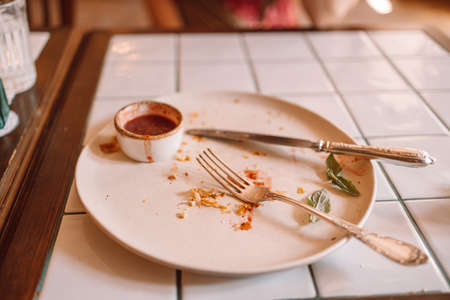 Empty dirty dish after breakfast with sauce and dessert fork. White modern dirty plate on wood cement backgroundの写真素材