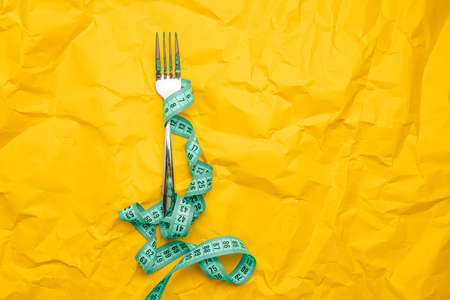 Iron fork with measuring tape on yellow paper texture background with a space paper for text. Crush paper. Mock up for body slimming, weight lossの写真素材