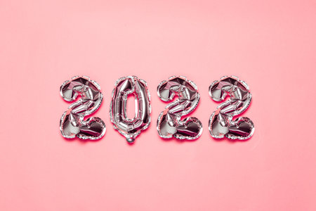 2022 silver foil balloons decor and Christmas snow with copy space on pink background. New Year and...