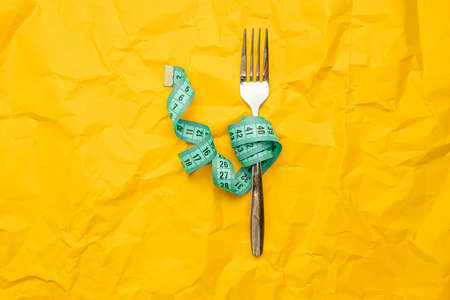 Food fork with measuring tape on yellow texture background. Crush paper. Diet and healthy food concept. Healthy lifestyle.の写真素材