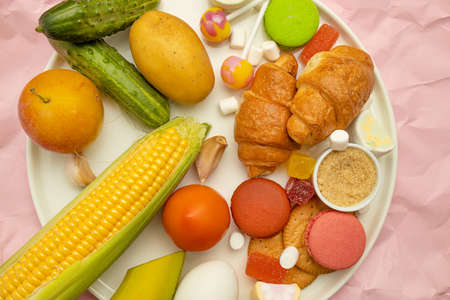Unhealthy foods on a colored background, top view. French croissant, candy on a stick, jelly candies, marshmallows, cookies and macarons on yellow bright backgroundの写真素材