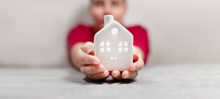 Cozy home house model with windows in hand palms on gray backgroundの写真素材