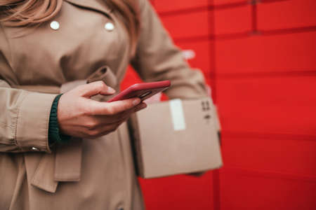 Young caucasian woman using automated self service post terminal machine or locker to deposit the parcel for storage. Online purchase delivery service concept.の写真素材