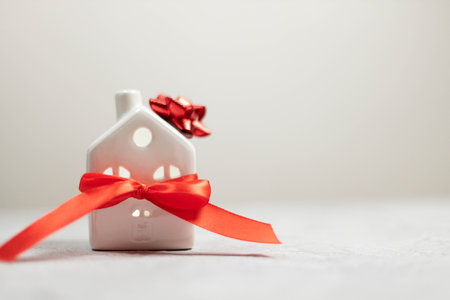 Christmas and New Year holiday. Miniature white toy house with red satin ribbon on white background. Flat lay, top view, copy spaceの写真素材