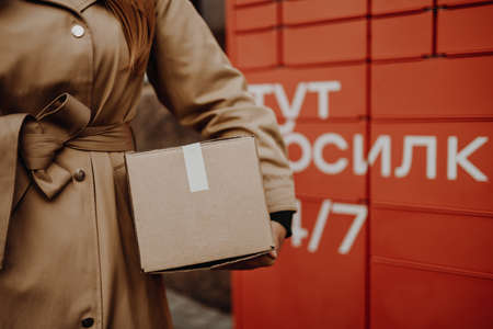 Woman picks up mail from automated self-service post terminal machine on the street. Parcel shipping service or delivery packaging conceptの写真素材