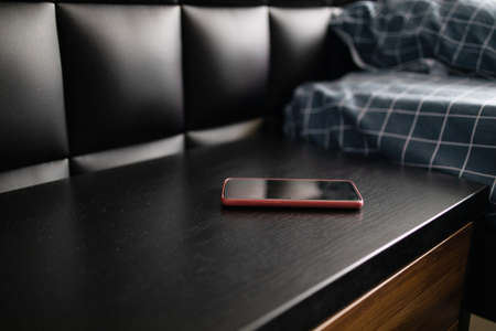 Black smartphone on the nightstand near the bed in the morning. Wood bedside table.の写真素材