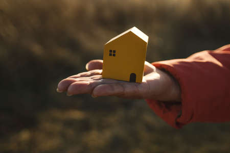 Close-up of female hand holding wooden white house model with autumn natural and a sunlight backgroundの写真素材