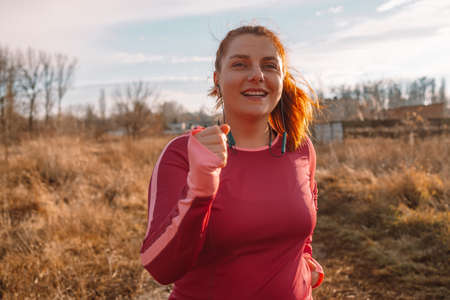 Happy sportive woman listens to music with headphones while jogging in nature in the morning.の写真素材