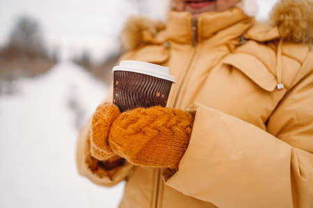 Female hand is holding paper coffee cup outdoors at winter cold frosty snowy day. Winter holidaysの写真素材