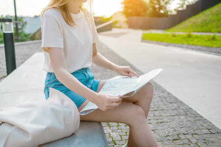 Woman hands with a city map sitting on a bench, travelling while hiking on a bright sunny day in...