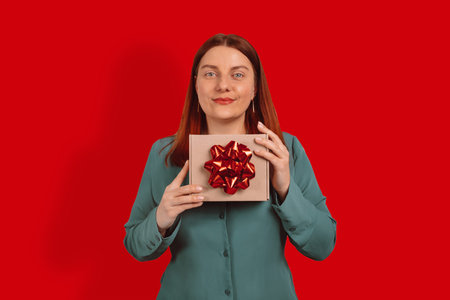Portrait of attractive happy funny girl holding gift box on red background, copy space. Birthday...