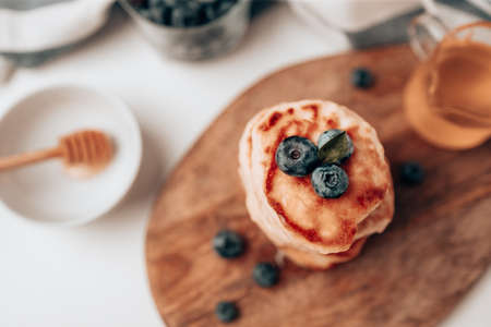 Wood plate of delicious pancakes with fresh blueberries and syrup on grey table against light backgroundの写真素材