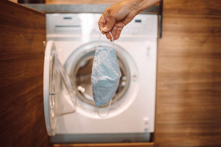 Female hand picking medical face mask in the washing machine for recyclingの写真素材