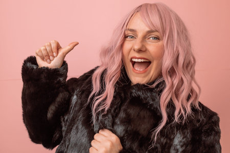 Happy and positive caucasian woman with pink curly hair wears black winter fur coat enjoying free...