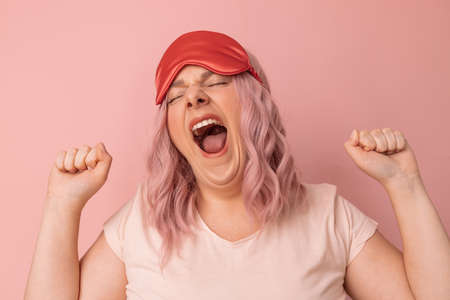 Beautiful relaxed young woman stretches, yawns as wants to sleep against pink background. Joy conceptの写真素材