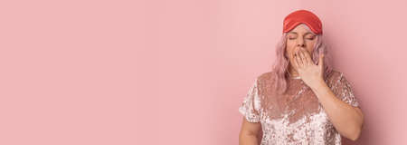 Sleepy tired woman wants to sleep, feeling exhausted, yawning, covering mouth with hand, wake-up early isolated over pink background.の写真素材