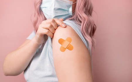 Beautiful young caucasian woman wearing protective mask  showing shoulder after vaccine getting. Booster dose, vaccine passport.の写真素材
