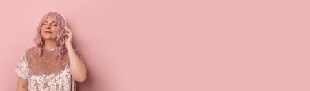 Positive woman with closed eyes smiling and listening to beautiful music enjoying the moment isolated over pink background. Banner with copyspace.の写真素材