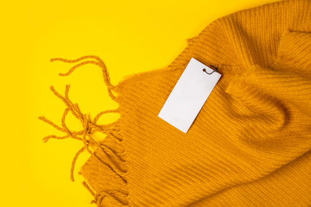 Beautiful yellow warm winter scarf with label tag mockup template on yellow background with space...