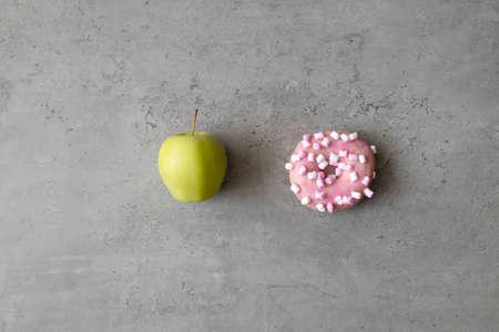 Pink donut and apple isolated on gray concrete background. Healthy and unhealthy food. Choice. Diet concept.の写真素材
